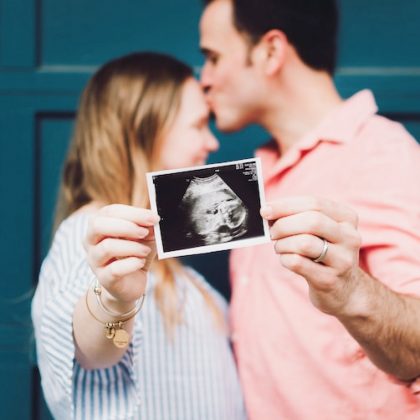 An image of a couple kissing whilst holding up a baby ultrasound image