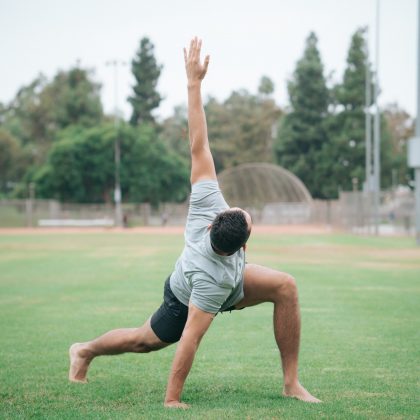 A man does a yoga pose in the middle of a field during day time