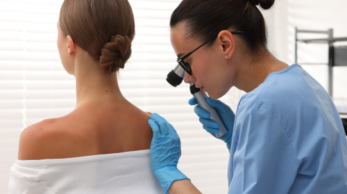 Doctor Examining Young Woman's Mole with Dermatoscope in Hospital