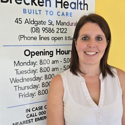 Dr Victoria Foster smiles at the camera in front of a Brecken Health sign.