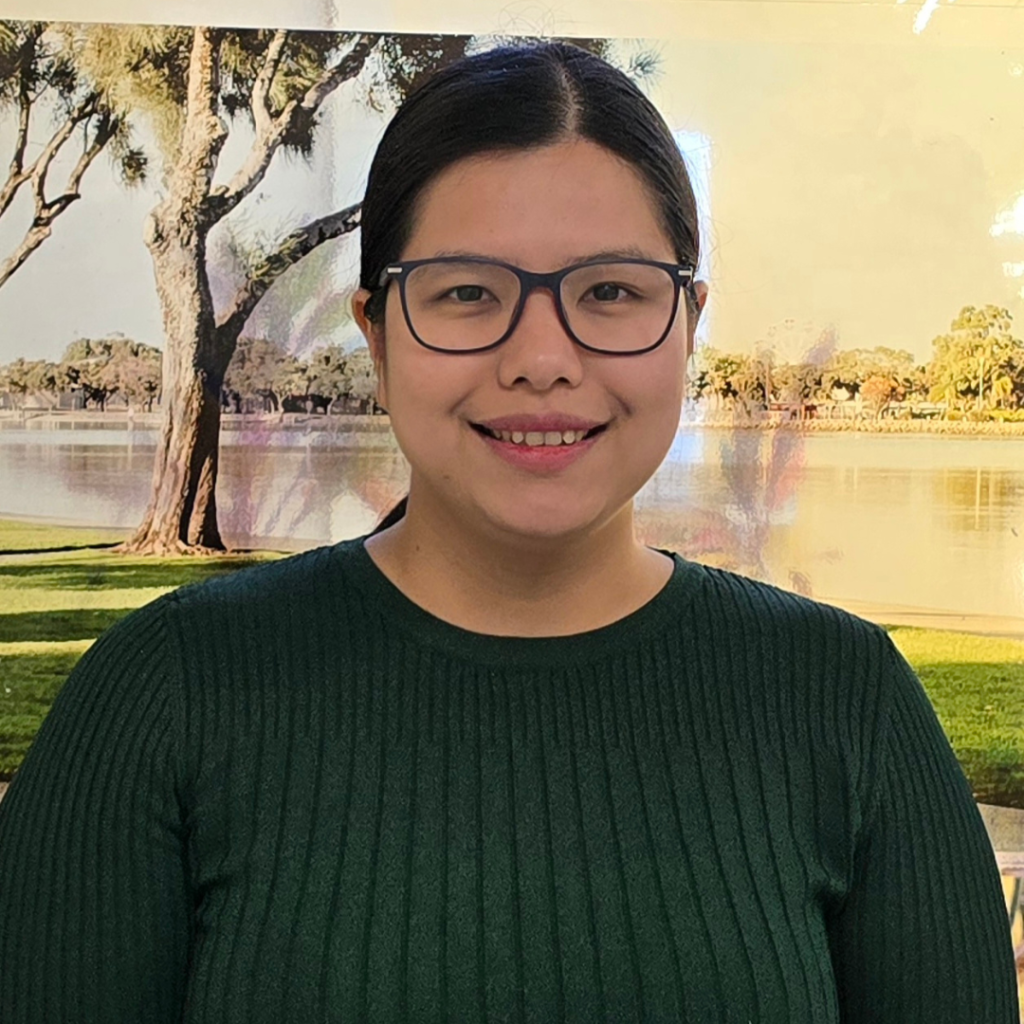 Dr Naychi Oo smiles at the camera. She has long dark hair that is in a ponytail and is wearing dark glasses.